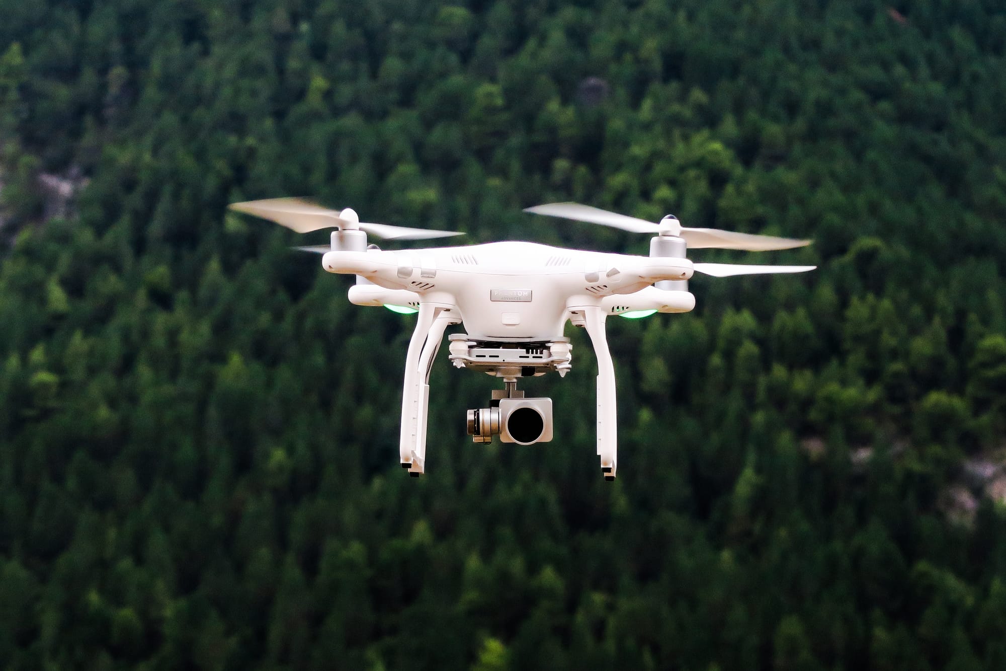 White quadcopter drone with a camera hovering in front of a forest, symbolizing childhood dreams of flight and vision from above.