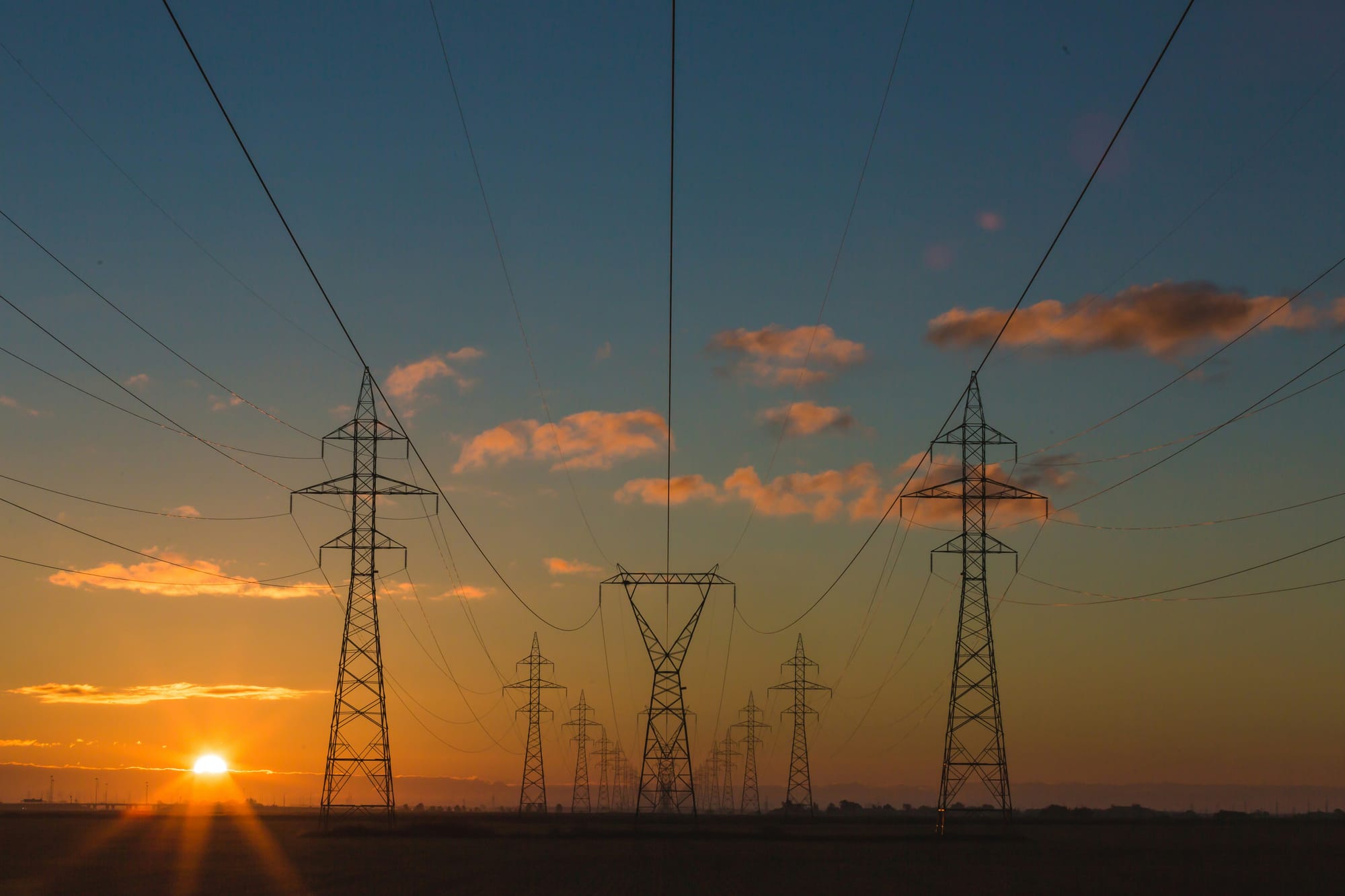 Sunset view of high-voltage power lines and pylons against a cloudy sky, symbolizing Nikola Tesla’s legacy and humanity’s ongoing quest to harness invisible forces.